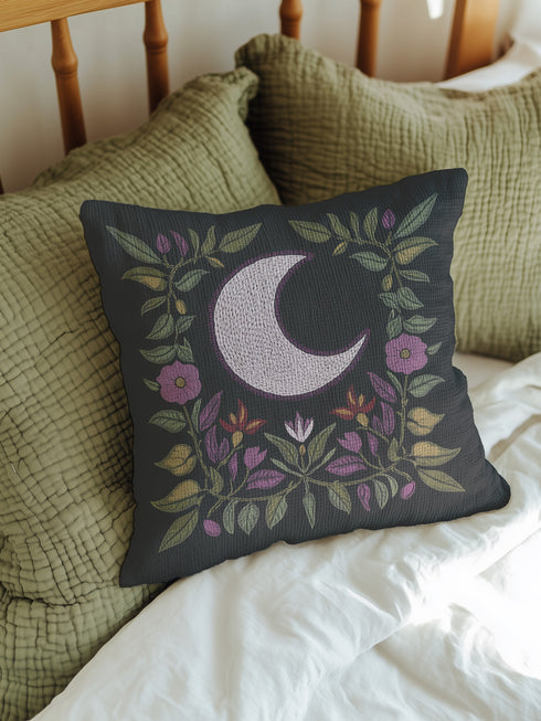 Black woven throw pillow with an embroidered crescent moon and floral pattern in soft ivory, green, purple, and gold, featuring a textured finish.